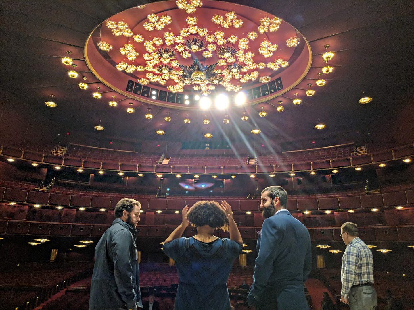 Michael Hewitt and fellow singers on stage at the Kennedy Center Opera House, looking out at the empty house under its crystal chandelier